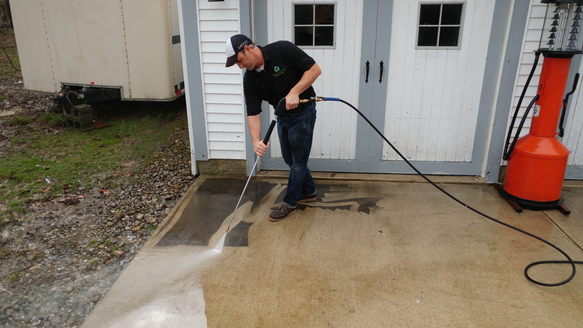 A man is washing his driveway with a hose.